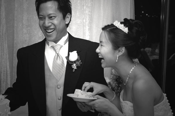Black and white photojournalistic photo of the bride and groom laughing after cutting the cake.