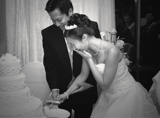 Black and white photojournalistic photo of the bride and groom cutting the cake.