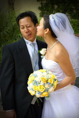 Groom reluctantly accepts a kiss from his bride with a bouquet of flowers in Montecito, Santa Barbara location.