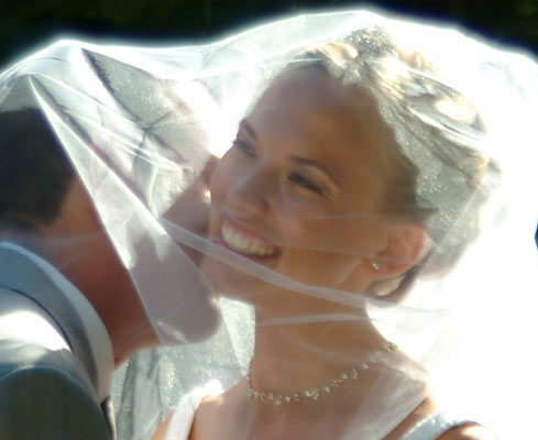 Groom sneaks a quick kiss on the brides cheek underneath her veil.